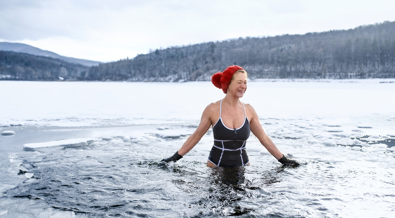 Een vooraanzicht van actieve senior vrouw in zwempak buiten in water in de winter, koude therapie concept. reinigen met water en kou