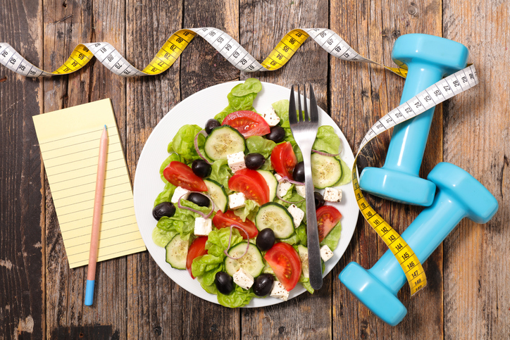 calorieen tellen, gezonde salade met gewichten en notitieblok en meetlint, houten achtergrond