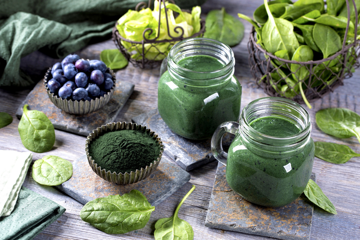 Groene smoothie met spirulina, spinazie en bosbessen met groene blaadjes en houten ondergrond