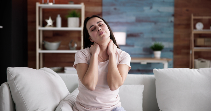 Jonge vrouw met nekpijn op een bank handen in de nek