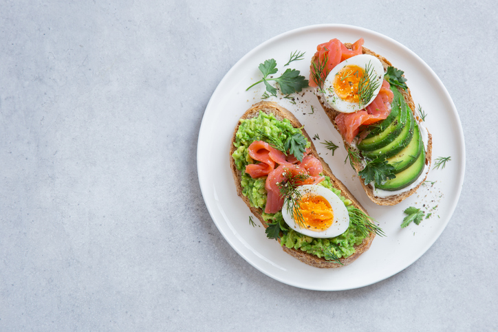 gezonde toast met avocado, zalm en ei grijze achtergrond