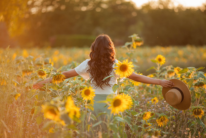 Jonge vrouw donker haar in zonnebloemveld, achteraanzicht zomerkwalen
