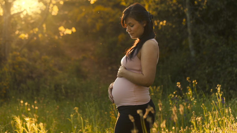 Zijaanzicht zwangere vrouw in de ondergaande zon in de natuur