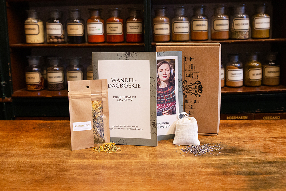 Sfeerbeeld van het pakket meditatiewandeling met zakje thee, lavendelzakje, wandeldagboekje en flyer in de winkel met houten ondergrond