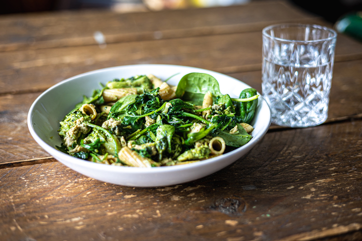 pasta met spinaziesaus met glas water, houten tafel